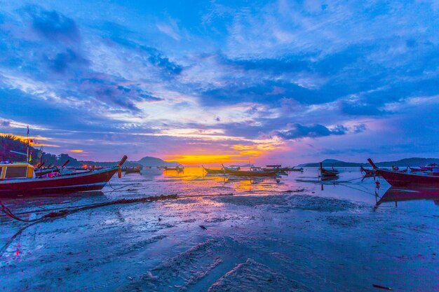 Fishing boats moored on sea against sky during sunset