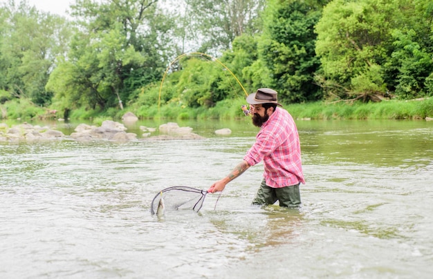 Fishing hobby Bearded brutal fisher catching trout fish with net If fish regularly you know how rewarding and soothing fishing is Fishing is an astonishing accessible recreational outdoor sport