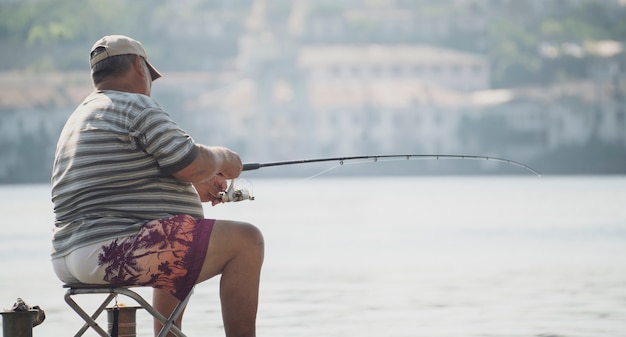 Увлечение рыбалкой, мужчина-рыбак сидит на набережной городской реки и ловит рыбу.