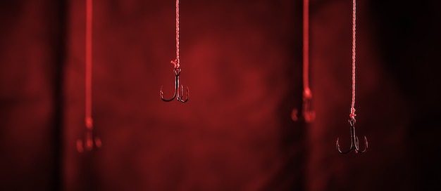 Fishing hooks hang on a dark background. Single hook in focus close-up.