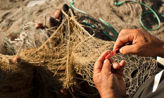 fishing net in the hands of fisherman, with needle and thread, grabs net with toes