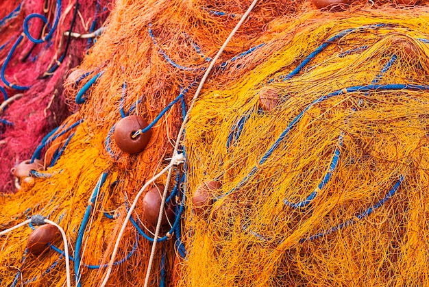 Fishing net of orange and yellow ropes and stack of buoys on the dock.