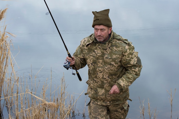 Fishing in the reeds for spinning on quiet water A man in camouflage clothes in cool weather