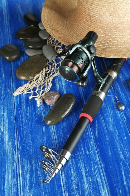 Fishing rod gumboots and hat on wooden table closeup