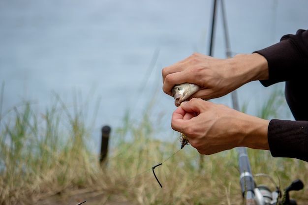 Foto primo piano della ruota della canna da pesca, uomo che pesca con una bellissima alba dietro di lui