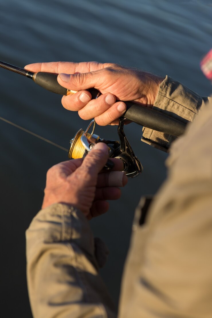 Fishing rod wheel closeup, man fishing with a beautiful sunset.