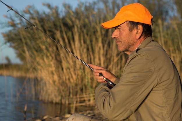 Foto pesca dell'uomo del primo piano della ruota della canna da pesca con un bel tramonto