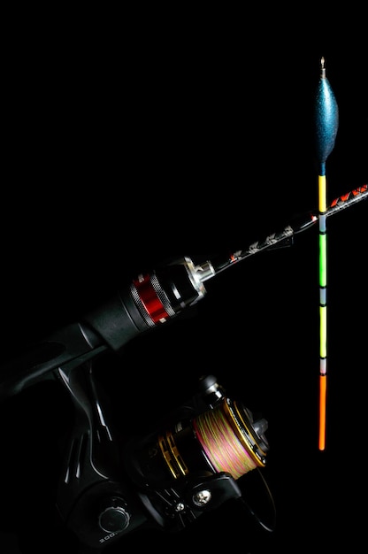 Fishing rod with a reel and colorful Fishing float on a black background.