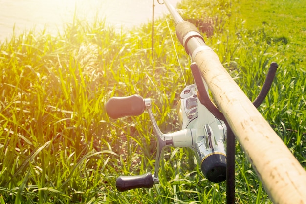 Canna da pesca con mulinello su un supporto vicino alla costa con la luce del sole.