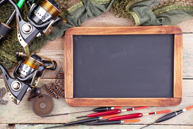 Fishing rods, blackboard and spinnings in the composition with accessories for fishing on the old surface on the table