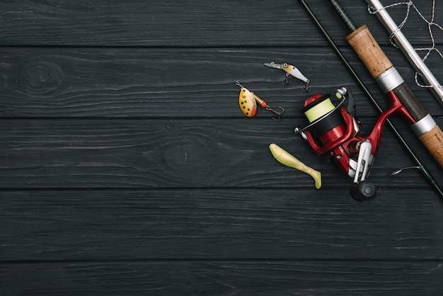 Рыболовные снасти - спиннинг, крючки и приманки на затемненном деревянном фоне. Вид сверху.