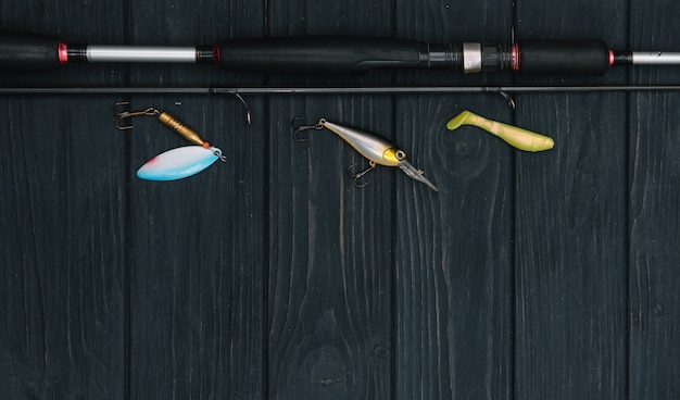 Fishing tackle - fishing spinning, hooks and lures on darken wooden background. Top view.