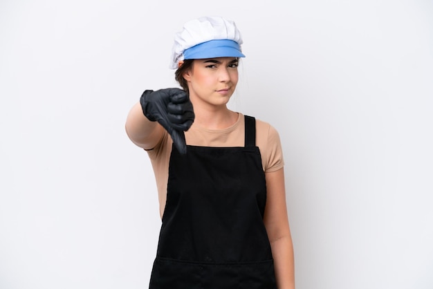 否定的な表現で親指を下に示す白い背景に分離されたエプロンを身に着けている魚屋のブラジル人女性