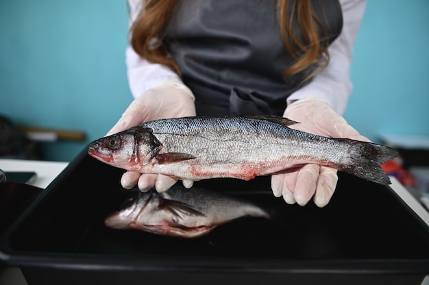 The fishmonger behind the counter holding a fresh fish in his hands. Focus on a silver sea bass in the hands of an unrecognizable merchant in a seafood market