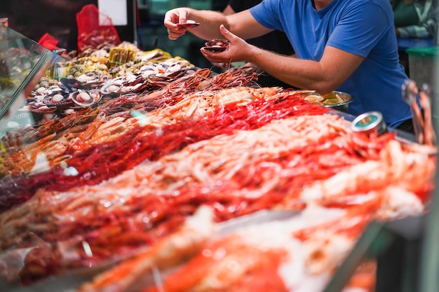 Рыботорговец продает рыбу на рынке морепродуктов. Сосредоточьтесь на правой руке, держащей устрицу.