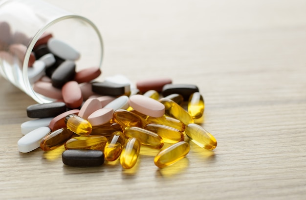 Fishoil capsules and Multivitamin supplements out of the small glass on the wooden table with copy space.