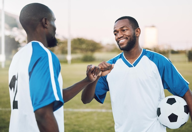 Fist bump soccer ball and black man with teamwork success of sports training on a grass field Football friends support and exercise with fitness motivation outdoor for health workout and smile