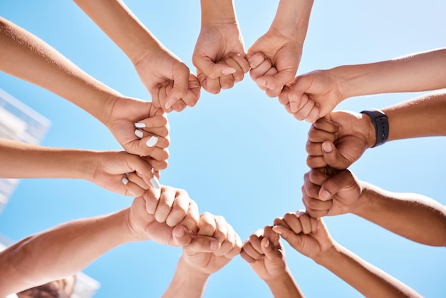 Fist hands circle and community support diversity people protest group and freedom fight on blue sky background Below solidarity teamwork and motivation for justice goal trust and society power