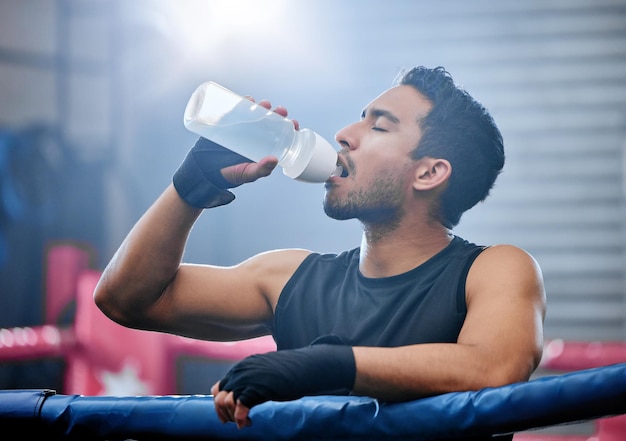 アクティブで健康的なボクサーが休憩時に水を飲み、定期的なワークアウト トレーニングやボクシング リングのエクササイズで水分を補給する キック ボクシングの戦いやスポーツの試合後のスポーティな運動選手または強い男
