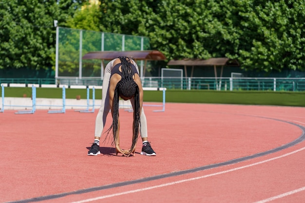 La donna afroamericana in forma gode di allungare il corpo in piedi sulla pista rossa dello stadio cittadino vicino al parco