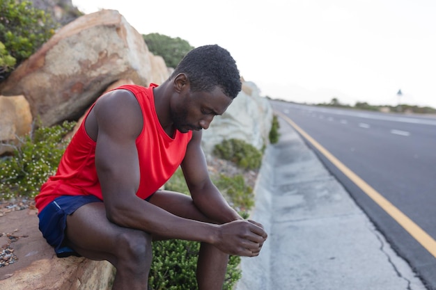 Fit Afro-Amerikaanse man in sportkleding zittend op een rots langs een kustweg. gezonde levensstijl, sporten in de natuur.