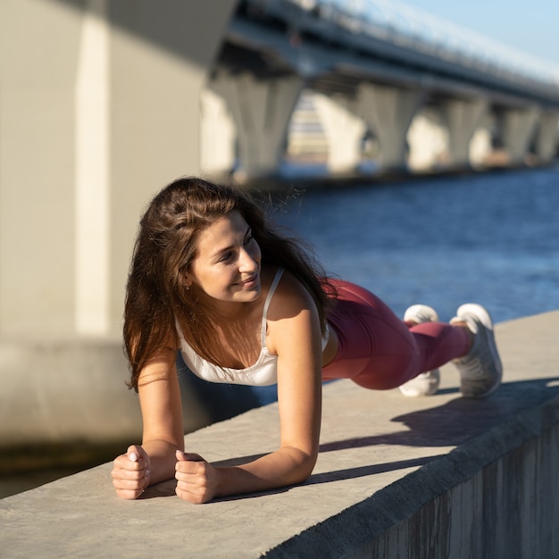 Montare la donna atletica facendo esercizio di plancia, allenamento cross-fit sull'argine