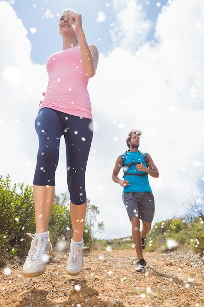 Fit attractive couple jogging down mountain trail against snow falling