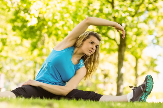 Fit blonde die zich uitstrekt in het park