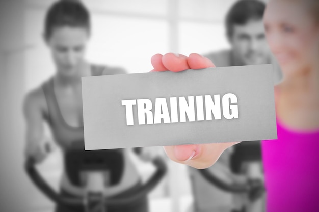 Photo fit blonde holding card saying training against spinning class in gym