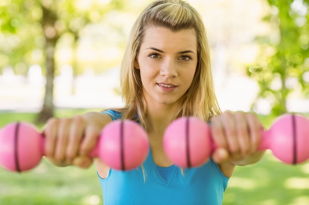 Fit blonde lifting dumbbells in the park