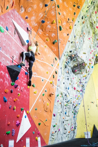 Fit blonde rock climbing indoors