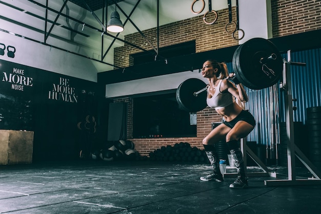 Foto fit blonde vrouw opleiding tillen een staaf gewichten in sportschool