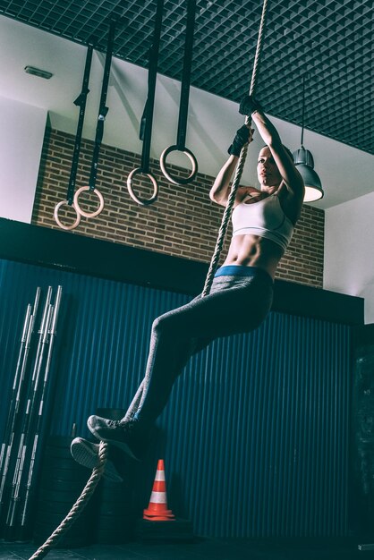 Fit blonde woman climbing the rope training working out in Gym