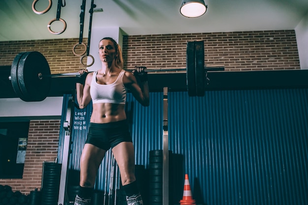 Fit blonde woman training lifting a bar weights in gym
