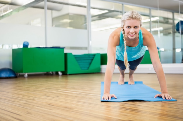 Fit blondine planking op mat in de fitness-studio