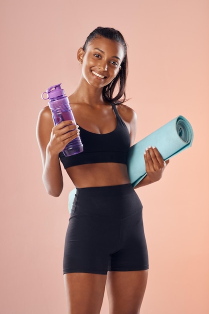 Fit body healthy and athletic woman in studio holding mat and water bottle for yoga pilates or exercise on pink background Portrait of sporty active or slim athlete ready for workout or training