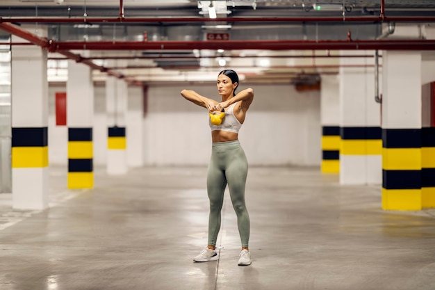 A fit bodybuilder is lifting kettle bell and exercising in urban interior