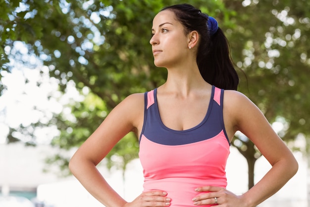 Fit brunette lachend met de handen op de heupen in het park