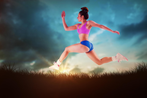 Fit brunette running and jumping against blue sky over grass