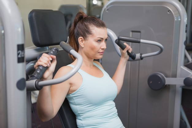 Fit brunette using weights machine for arms