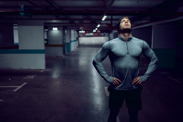 fit caucasian sportsman in active wear standing in garage with hands on hips and resting.