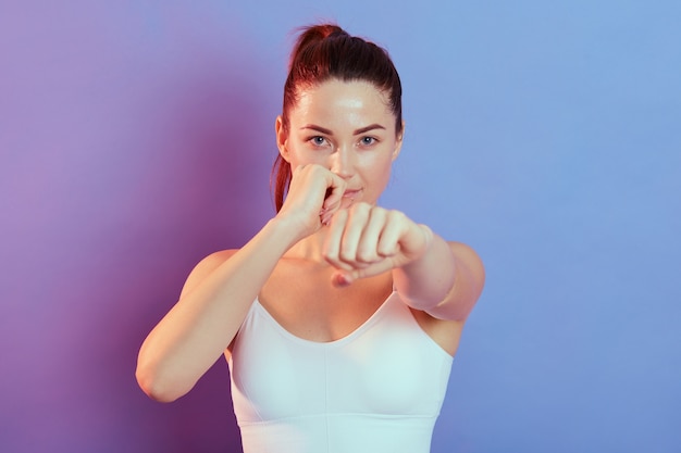 Montare la donna caucasica nella boxe degli abiti sportivi su sfondo colorato in luce al neon, boxer femmina attraente che lavora e si allena. sport, stile di vita sano, movimento.