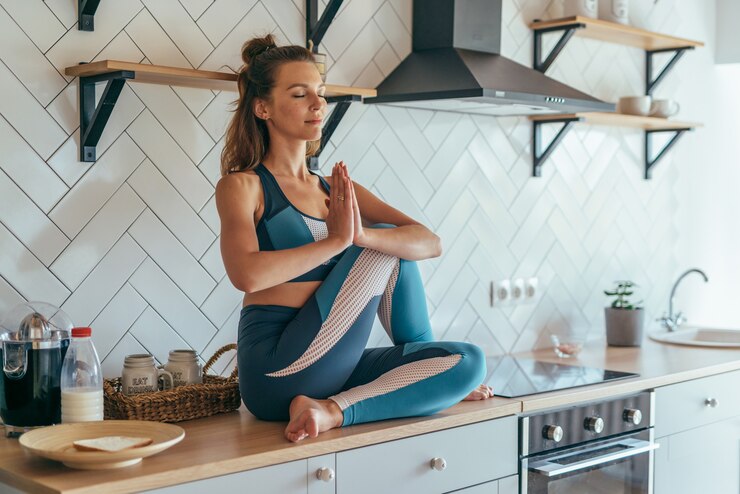 Photo fit concentrated caucasian woman sitting on talbe in kitchen and meditating.