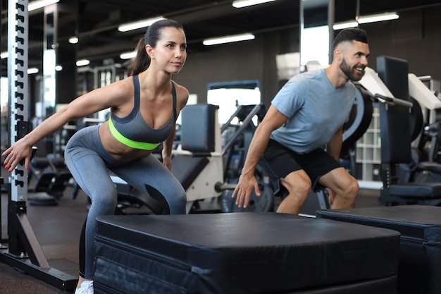 Fit couple doing jumping squats in crossfit gym.