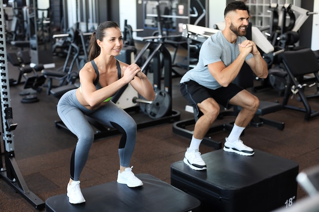 Fit couple doing jumping squats in crossfit gym.