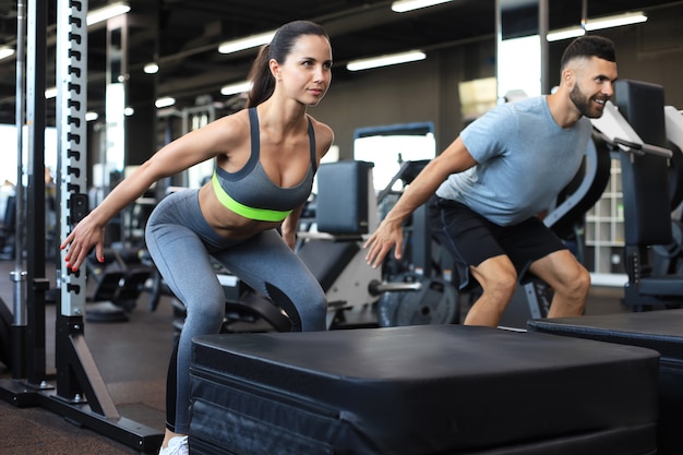 Fit couple doing jumping squats in crossfit gym.