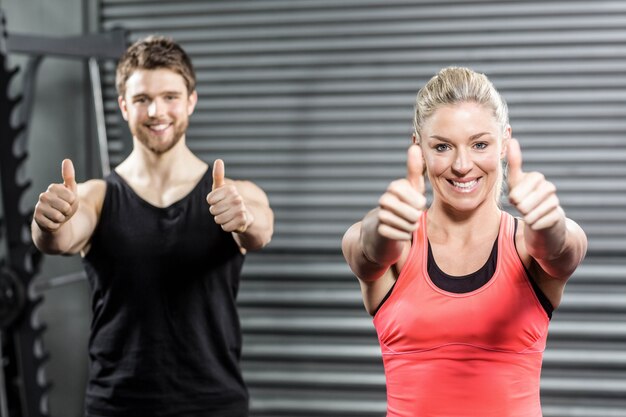 Fit couple with thumbs up at crossfit gym