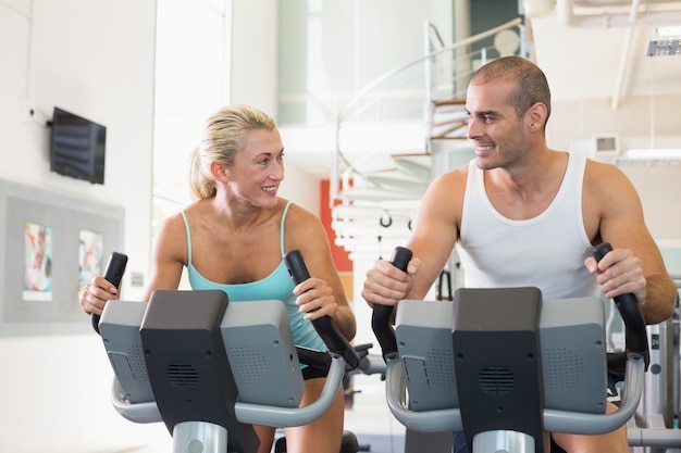 Fit couple working on exercise bikes at gym