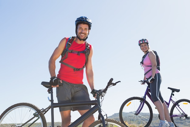 Fit cyclist couple standing at the summit smiling at camera