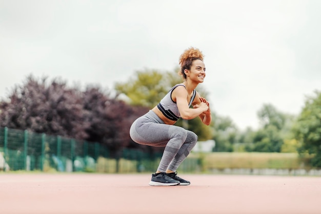 A fit dedicated sportswoman is doing squats endurance in the stadium in rainy weather